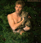 Topless dude standing in a Christmas tree and holding a cat.