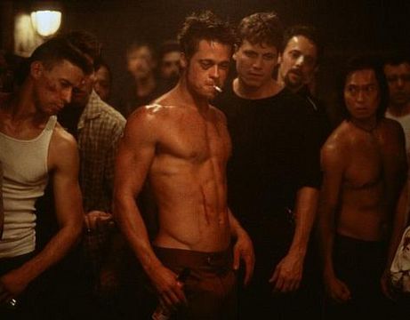 A topless and bloody Brad Pitt smoking a cigarette, surrounded by other sweaty guys in a scene from Fight Club.